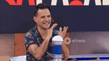 a man applauds in front of a screen that says eltrece