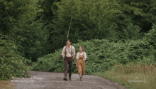 a man and a woman walking down a dirt road in a hallmark ad