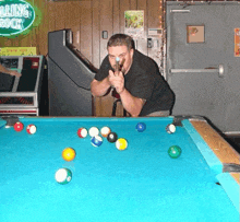 a man is playing pool on a pool table with a rolling rock sign in the background