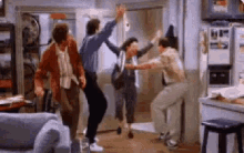 a group of people are dancing in a living room with a refrigerator in the background .
