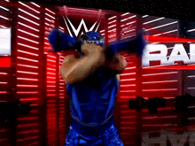 a man in a blue wrestling outfit is standing in front of a red wall with the word raw on it