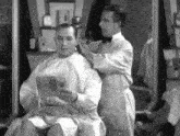 a man is getting his hair cut by a barber in a barber shop while holding a magazine .