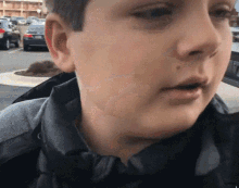 a close up of a young boy 's face with a car parked in the background ..
