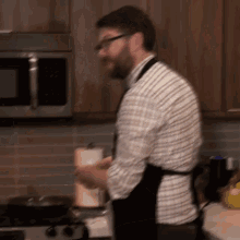 a man in a plaid shirt and apron is standing in a kitchen