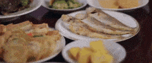 a table topped with plates of food including fish , vegetables and bread .