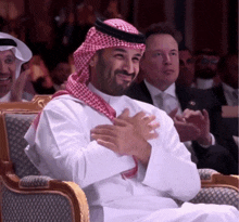 a man wearing a keffiyeh sits in a chair with his hands folded
