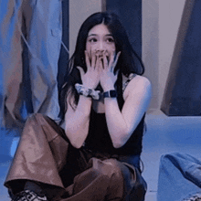 a woman covering her mouth with her hands while sitting on the floor