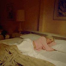 a woman in a pink shirt is laying on a bed with white sheets