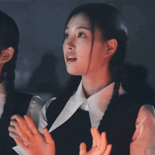a woman in a white shirt and black vest looks surprised