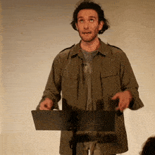 a man in a green jacket stands at a podium with his hands outstretched