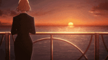 a woman in a black suit stands on a railing overlooking the ocean at sunset
