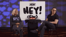 two people sit in front of a sign that says " hey "