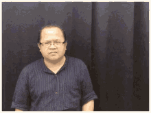 a man wearing glasses and a blue striped shirt is making a funny face .