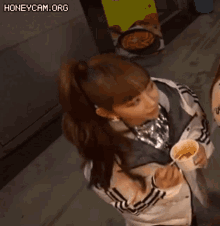 a girl in a ponytail is holding a cup of food .
