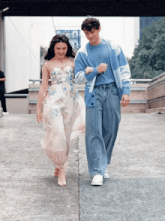 a man and a woman are walking down a sidewalk and the woman is wearing a white dress