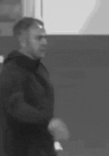 a black and white photo of a man in a black jacket standing in a room .