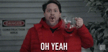 a man in a red jacket is holding a glass in his hand and saying `` oh yeah '' .