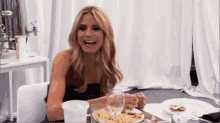 a woman is sitting at a table eating french fries and drinking wine .