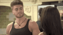 a man in a black tank top is standing next to a woman in a kitchen .