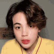 a close up of a person 's face wearing a yellow shirt and a red necklace .