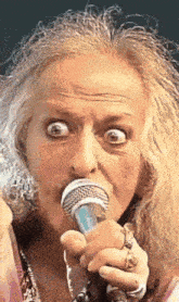 a close up of a woman singing into a microphone with her eyes wide open