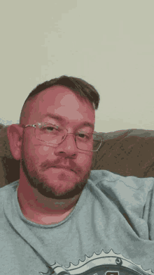 a man wearing glasses and a grey shirt with the letter g on it is sticking his tongue out