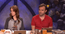 a man and a woman are sitting at a table with a tablet and a bottle of beer