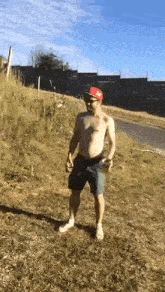 a shirtless man in a red hat and shorts is standing in a field .