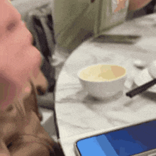 a person sitting at a table with a cell phone and a bowl