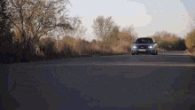 a blue ford car is driving down a country road