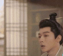 a man with a bun on his head is standing in front of a window in a room .