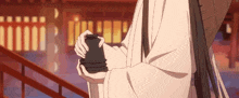 a person in a white robe is holding a black cup in their hand .