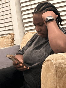 a woman wearing a watch is sitting on a couch looking at her cell phone