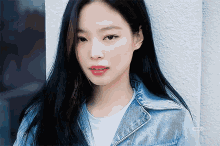 a woman with long black hair wearing a denim jacket and a white shirt looks at the camera