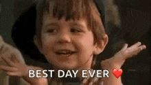 a little boy is smiling and saying `` best day ever '' with his arms outstretched .