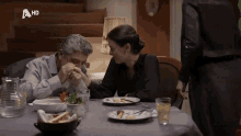 a man and a woman are sitting at a table with a hd logo on the bottom right