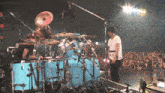 a man playing drums in front of a crowd with the number 0 on the bottom right