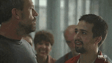 two men are standing next to each other and talking to each other .