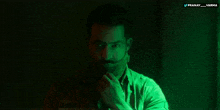 a man with a beard and mustache is in a dark room with a green light behind him that says pranay and varha