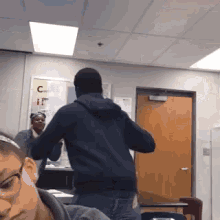 a man in a black hoodie is standing in front of a woman in glasses