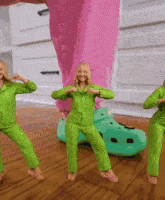 three women in green jumpsuits are dancing in front of a large croc