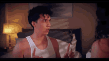 a man in a white tank top is talking to a woman in bed