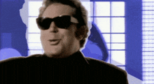 a man wearing sunglasses and a black suit is smiling