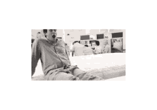 a black and white photo of a man sitting on a bed in a hospital .