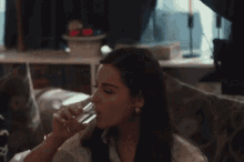 a woman is drinking water from a glass while sitting on a couch