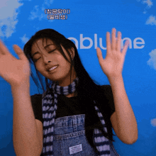 a woman wearing overalls and a scarf stands in front of a blue background with the word bluline on it