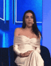 a woman in a white dress is sitting in a chair in front of a blue background .