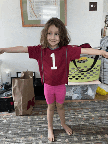 a little girl wearing a maroon shirt with the number 1 on it