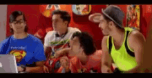 a man wearing a superman shirt sits next to a man wearing a yellow tank top