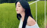 a woman with long black hair is standing in a grassy field